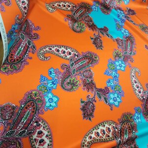 May include: Orange fabric with a paisley pattern in shades of pink, blue, green, and black. The fabric has a satin finish.