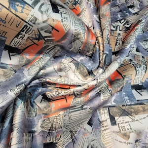 Könnte beinhalten: Ein grauer Stoff mit einem bunten Druck aus überlappenden Texten und abstrakten Formen. Der Druck zeigt eine Mischung aus schwarzen, weißen, orangefarbenen und blauen Farben.