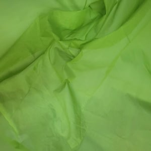 Può includere: Un primo piano di un tessuto verde chiaro con una texture liscia. Il tessuto è piegato e drappeggiato, creando pieghe e rughe morbide.