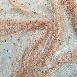 Può includere: Primo piano di un tessuto trasparente color pesca con un delicato motivo a rete e paillettes iridescenti sparse.