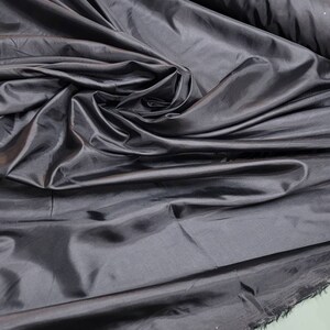 May include: A close-up of a smooth, black fabric with a silky sheen. The fabric is draped and folded, showcasing its texture and drape.
