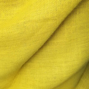 Peut inclure: Un gros plan sur un tissu de jute jaune avec une texture tissée. Le tissu est plié en deux, créant une ligne diagonale à travers l'image.