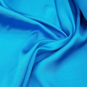Könnte beinhalten: Nahaufnahme eines leuchtend blauen Stoffes mit glatter, seidenartiger Textur. Der Stoff ist gefaltet und drapiert und erzeugt weiche, fließende Linien.