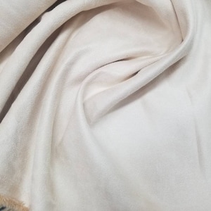Peut inclure: Gros plan sur un tissu doux de couleur crème avec une texture duveteuse. Le tissu est plié et drapé, révélant sa surface lisse et son léger brillant.