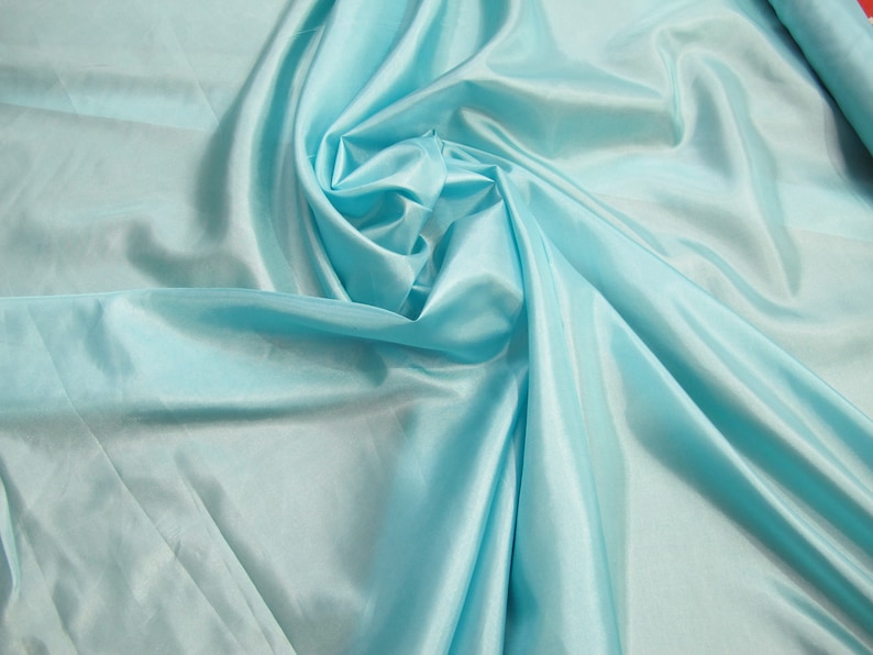 May include: A smooth, light blue fabric with a silky texture. The fabric is draped and folded, creating soft curves and folds.