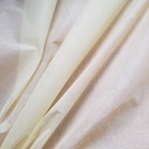 Può includere: Primo piano di un tessuto trasparente di colore giallo pallido, piegato e drappeggiato, che mette in evidenza la sua texture delicata e la sua qualità traslucida.