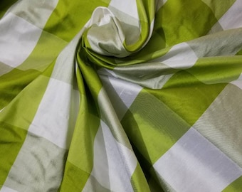 May include: Green and white checkered fabric with a silky texture. The fabric is folded and draped, showcasing its soft and flowing nature.