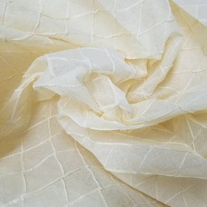 Può includere: Tessuto trasparente color crema con un motivo a forma di diamante. Il tessuto è testurizzato e ha una leggera lucentezza.