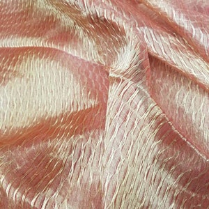Peut inclure: Gros plan sur un tissu rose et or avec un motif texturé et tissé. Le tissu est doux et transparent, avec un léger chatoiement.