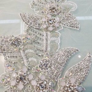 May include: A delicate floral design embroidered with sparkling rhinestones and pearls. The design features a cluster of flowers with leaves and stems, all adorned with shimmering embellishments.