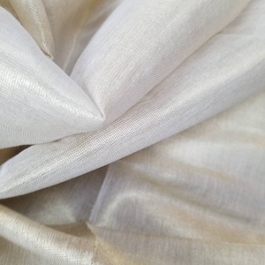 May include: Close-up of a sheer, ivory-colored fabric with a subtle shimmer. The fabric is folded and draped, showcasing its delicate texture.