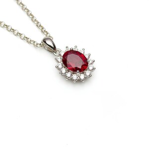 May include: A silver necklace with a red oval gemstone surrounded by smaller white gemstones.
