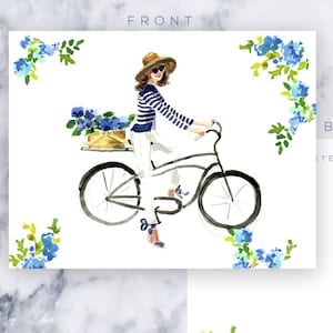 May include: A watercolor illustration of a woman riding a bicycle with a basket of blue flowers on the back. The background is white with a blue floral border.