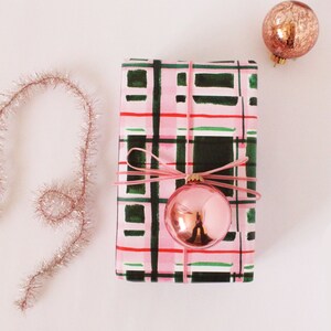 May include: A pink and green plaid gift wrap with a pink ribbon and a pink and gold ornament.