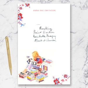 May include: A white sheet of paper with a floral design at the top and bottom. The text "ANNA RAE SMITHSON" is at the top of the page. The text "Darling Saint Eulalia,  haunt me always. Most et claudor." is written in black ink. A watercolor illustration of a woman sitting on a stack of books is in the center of the page.