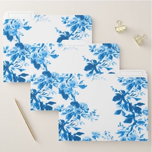 May include: Three white file folders with a blue floral design. The floral pattern features blue roses and leaves. Two gold binder clips and a gold pen are also visible.