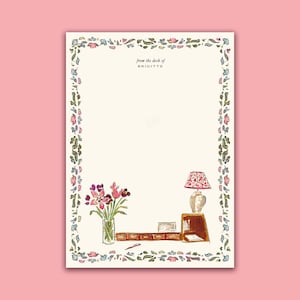 May include: A white card with a floral border and the text "from the desk of BRIGITTE". The card features a watercolor illustration of a vase of flowers, a lamp, and a desk with a book and a pen.