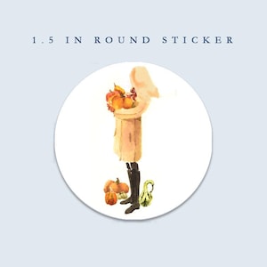 May include: A round sticker with a watercolor illustration. The image features a person in a tan coat holding pumpkins, with additional pumpkins and gourds at their feet. The text "1.5 in round sticker" is at the top.