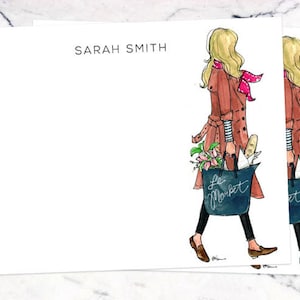 May include: A set of two blank stationery cards featuring a woman in a brown coat and red scarf carrying a bag that says "Le Market". The cards have the name "SARAH SMITH" printed at the top.