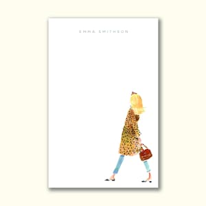 May include: A white notepad with the text "EMMA SMITHSON" at the top. The notepad features a watercolor illustration of a woman in a leopard print coat, blue jeans, and carrying a red handbag. The woman is walking.