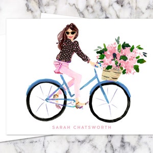 May include: A watercolor illustration of a woman wearing sunglasses and a polka dot shirt riding a blue bicycle with a basket of pink flowers.