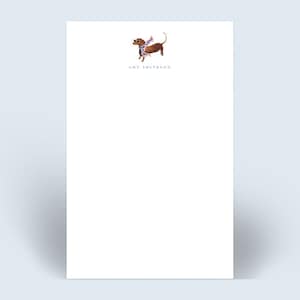 May include: White notepad with a brown dachshund wearing a blue and white scarf. The notepad has the name "Amy Smithson" printed at the bottom.