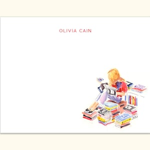 May include: White stationery with the name "OLIVIA CAIN" in red. A watercolor illustration depicts a person reading, surrounded by stacks of books. The person is wearing a red shirt and blue jeans.