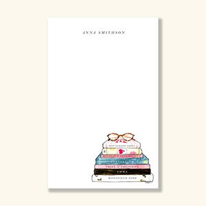 May include: White notepad with the name "ANNA SMITHSON" at the top. A stack of books with titles like "Northanger Abbey" and "Pride & Prejudice" is illustrated at the bottom, topped with eyeglasses.