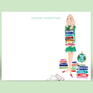 May include: A white card with the name "SUSAN THORNTON" printed in teal blue at the top. A woman with blonde hair is illustrated holding a stack of colorful books. There are stacks of books and a globe on a table in the background.