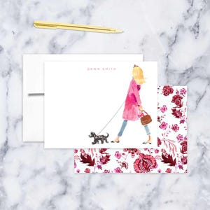 May include: A white card with a pink floral pattern border. The card features a watercolor illustration of a woman in a pink coat walking a black dog. The woman is carrying a brown purse. The text "DAWN SMITH" is printed in pink at the top of the card.