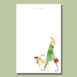 May include: A white notepad with the name "PAMELYN" printed at the top. The notepad features a watercolor illustration of a woman in a green coat walking a dog with a green scarf.