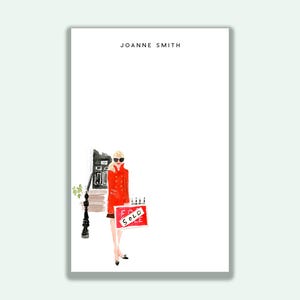 May include: Illustration of a woman in a red coat holding a "SOLD" sign. The artwork is on a white background with the text "JOANNE SMITH" at the top. The woman is standing in front of a building.