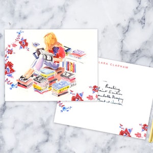 May include: A watercolor illustration of a woman sitting on a stack of books, reading a book. The illustration is surrounded by a floral border. The text "Lara Clapham" is in the upper right corner of the illustration. The text "Reading Saint Exupery,  Gabrielle Murray,  and Elizabeth Gilbert" is in the lower right corner of the illustration.