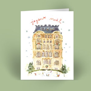 May include: A watercolor illustration of a building with a festive wreath on the door. The building is decorated with snow and people are ice skating in front of it. The text "joyeux noël" is written in red at the top of the card.