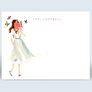 May include: Watercolor illustration of a woman in a flowing dress with butterflies. The artwork is on a white card with the name "TORI CAMPBELL" in red. The woman is wearing a white dress with a light blue accent.