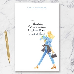 May include: A white notebook with the text "SUSAN THORNTON" at the top and the handwritten text "Nourishing.  Soul is within the subtle things.  Lost & found." in black ink. A watercolor illustration of a woman in blue jeans and a blue and white plaid shirt walking with a bouquet of blue flowers and a black handbag.