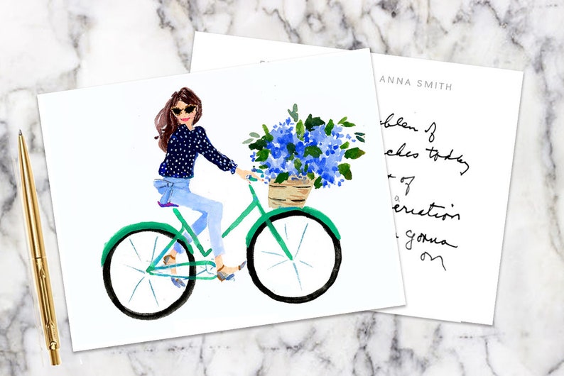 K&ouml;nnte beinhalten: Aquarellillustration einer Frau auf einem gr&uuml;nen Fahrrad mit einem Korb voller blauer Blumen. Die Frau tr&auml;gt eine Sonnenbrille, ein marineblaues Polka-Dot-Hemd und Jeans. Ein goldener Stift und eine Karte mit handschriftlichem Text sind ebenfalls zu sehen.