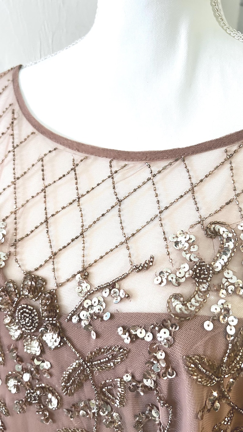 May include: Close-up of a formal dress bodice. The sheer overlay features a diamond pattern created with small, bronze-colored beads. Floral and leaf designs are embellished with sequins and beads in shades of silver and bronze.