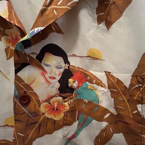 May include: A white button-up shirt with a tropical print featuring a woman, a parrot, and brown palm leaves. The shirt has a pocket on the left side.