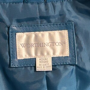 K&ouml;nnte beinhalten: Nahaufnahme des Innenraums einer teal-farbenen Lederjacke. Das Worthington-Etikett ist sichtbar, mit Text, der Gr&ouml;&szlig;e und Herkunft angibt. Die Jacke hat eine Schlaufe am Kragen und ein gestepptes Futter.