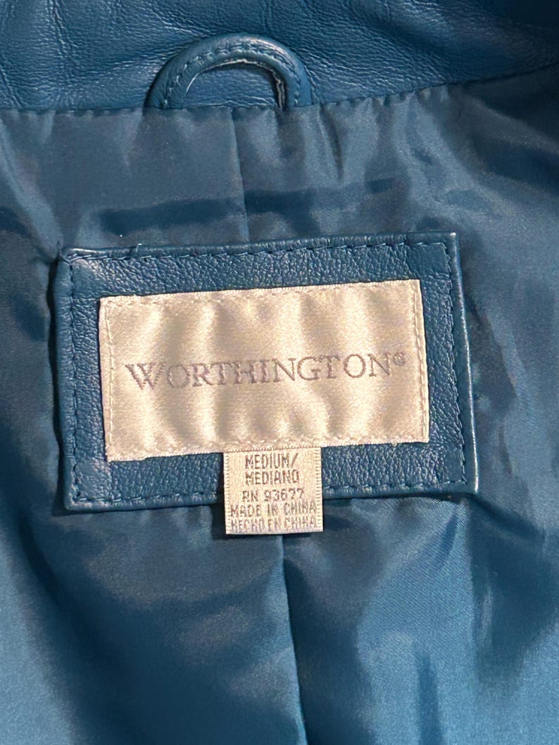 K&ouml;nnte beinhalten: Nahaufnahme des Innenraums einer teal-farbenen Lederjacke. Das Worthington-Etikett ist sichtbar, mit Text, der Gr&ouml;&szlig;e und Herkunft angibt. Die Jacke hat eine Schlaufe am Kragen und ein gestepptes Futter.