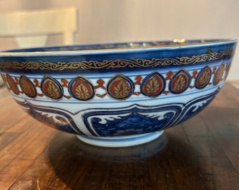 May include: A decorative blue and white ceramic bowl with intricate gold and red floral patterns. The bowl has a wide rim and a detailed design around the exterior, showcasing a blend of traditional artistry and elegant design.