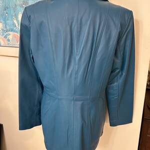 K&ouml;nnte beinhalten: T&uuml;rkisfarbener Lederblazer mit Reverskragen und langen &Auml;rmeln. Die R&uuml;ckseite der Jacke hat vertikale N&auml;hte f&uuml;r eine ma&szlig;geschneiderte Passform. Die Jacke wird auf einer Schaufensterpuppe pr&auml;sentiert.