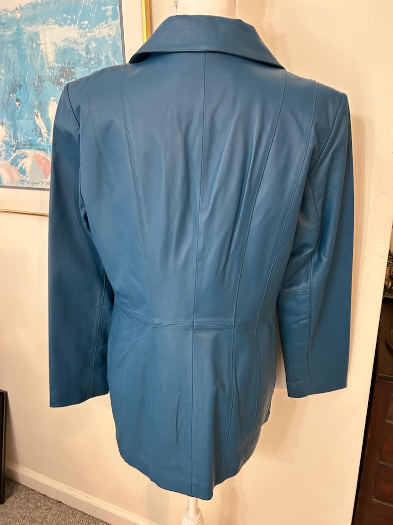 K&ouml;nnte beinhalten: T&uuml;rkisfarbener Lederblazer mit Reverskragen und langen &Auml;rmeln. Die R&uuml;ckseite der Jacke hat vertikale N&auml;hte f&uuml;r eine ma&szlig;geschneiderte Passform. Die Jacke wird auf einer Schaufensterpuppe pr&auml;sentiert.