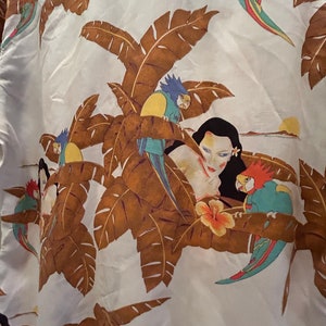 May include: White fabric with a tropical print featuring brown palm leaves, a woman's face, and colorful parrots. The parrots are blue, green, yellow, and red.