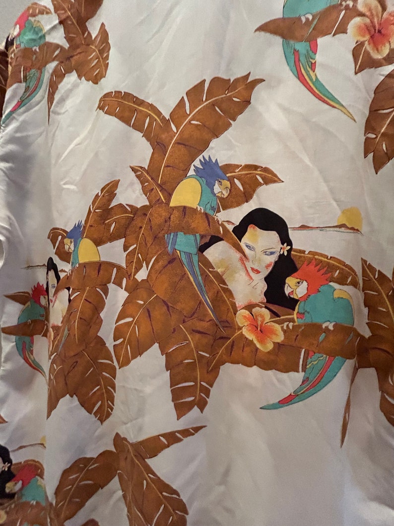 May include: White fabric with a tropical print featuring brown palm leaves, a woman's face, and colorful parrots. The parrots are blue, green, yellow, and red.