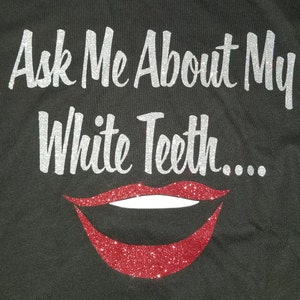 K&ouml;nnte beinhalten: Ein schwarzes T-Shirt mit dem Text "Ask Me About My White Teeth..." in silbernen Glitzerbuchstaben. Unter dem Text befindet sich ein roter Glitzermund mit wei&szlig;en Z&auml;hnen.