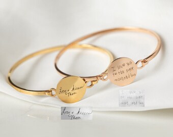 Puede incluir: Dos pulseras de brazalete de oro con dijes redondos grabados. Un dije dice "Te amo hasta la superluna y de regreso". El otro dije dice "Amor y besos Mamá".
