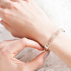 Op de afbeelding: Een zilveren armband met Romeinse cijfers op een witte achtergrond.