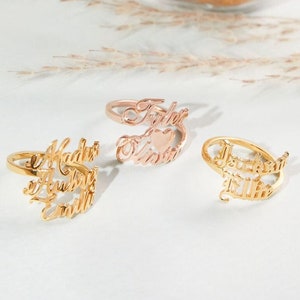 May include: Three gold rings with names inscribed on them. The rings are stacked on a white surface. The names on the rings are "Maddie Aubrey Emily", "Tyler Vinita", and "Jackson & Lily".